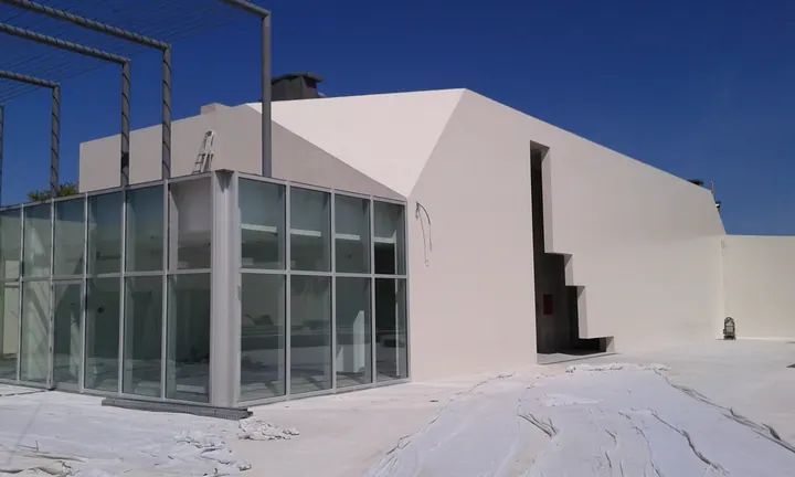 Pavilhão envidraçado em construção junto a volume branco